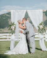 bride and groom share first kiss, draped wedding arch with flowers, mountain views